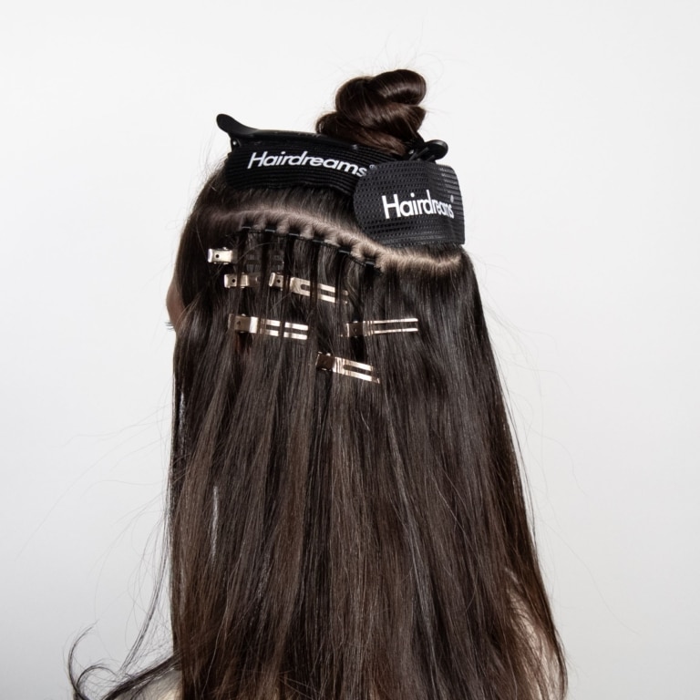 A hairdresser attaches the human hair weave to the client's own brown hair using clips.